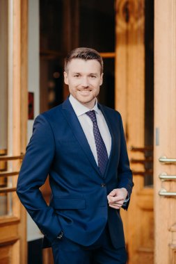 Çekici erkek yönetici resmi olarak dışarıda, el ele tutuşuyor, olumlu bir ifadeye sahip, ofise yakın duruyor, başarıya seviniyor, başarıya güveniyor. Erkek avukat kapıların yanında duruyor.