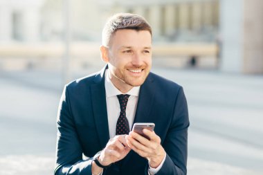 Çekici erkeğin düşünceli ifadesiyle yatay çekim, internat web sitesinde bilgi aramak için modern cep telefonu kullanıyor, yüksek hızlı 4G internete bağlanıyor, çevrimiçi para kazanıyor.