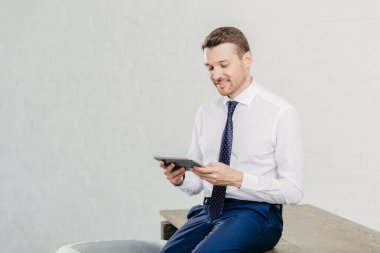 Olumlu erkek yatırımcı beyaz gömlek giyer, kravat, masaya oturur, dokunmatik yüzey, kablosuz internet'e bağlı yeni uygulama yükler. Başarılı bir iş adamı bildirim modern cihaz üzerinde okur