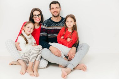 Beyaz arka plan üzerinde hep birlikte mutlu dostane aile poz fotoğraf. Dost görünümlü Anne, baba ve iki kızı, yere otur, neşeli ifadeler. Beraberlik kavramı