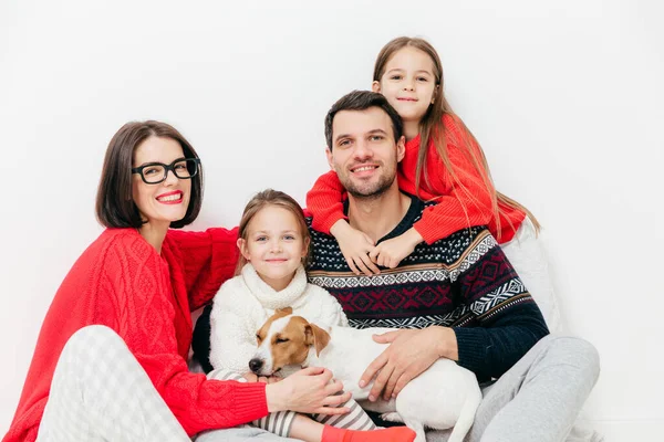 Portrait of happy family members with positive expressions, cuddle and support each other, have good relationship. Delighted father, mother, two sisters and small puppy pose together indoor.