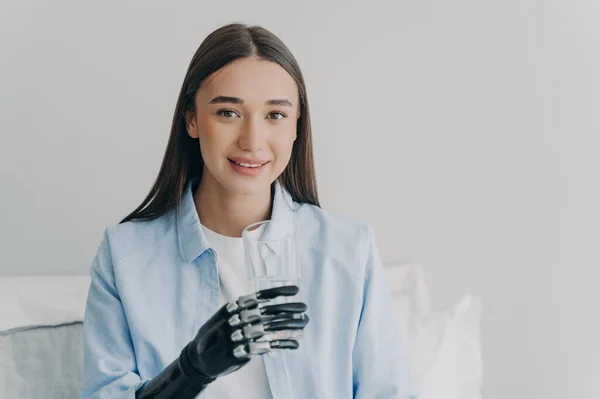 Happy disabled girl grasps a glass with myoelectric hand. High technology prosthesis. Nervous control sensored hand. European woman is smiling. Technology and science innovation concept.