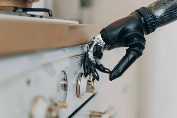 Carbon prosthetic hand of disabled person is switching a stove on at kitchen. Amputee with high technology artificial arm at home. Functions of modern bionic prosthesis. Routine of disabled person.