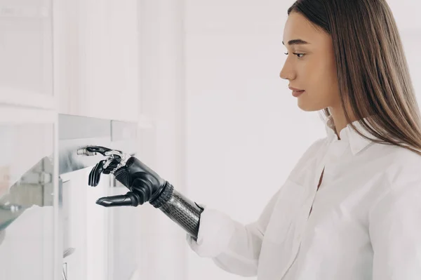 European handicapped woman is cooking. Robotic cyber hand is switching oven on at kitchen. Amputee is using high technology futuristic bionic prosthesis. Software in fingers and wrist joint.