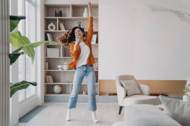 Young woman is singing, dancing and jumping. Carefree girl with smartphone having fun crazy and screaming at home. Favourite song and relaxation. Concept of emotional expressions and rebellion.