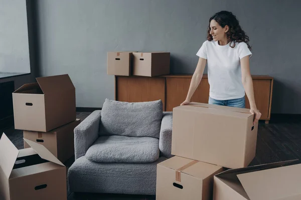 Happy european woman relocates alone. Proud single lady in casual outfit moves. Cardboard boxes on floor. Real estate purchase and mortgage. Delivery service ordering for the boxes unloading.