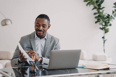 İş adamının evrak işleri var. Mutlu Adam 'ın bilgisayarında video görüşmesi var ve kalem ile veri kağıtlarını gösteriyor. Freelancer merkez ofiste çalışıyor. Uzak Afrikalı Amerikan işçisi..