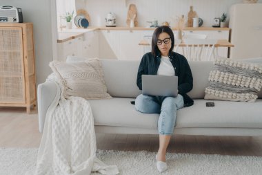 Bilgisayarda daktilo eden konsantre bir kız. İspanyol iş kadını evden başlayarak yeni bir proje üzerinde çalışıyor. Bayan Freelancer dizüstü bilgisayarla kanepede oturuyor. Modern dairede rahat bir iş yeri.