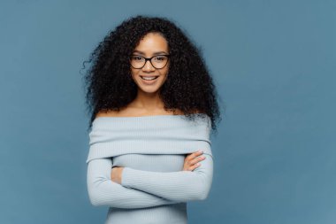 Mutlu genç kadın yarım uzunlukta çekim emin yüz ifadesi vardır, kollar katlanmış tutar, şık kazak giymiş, iş arkadaşları ile tanışmak için mutlu, mavi stüdyo duvarında izole, metin için boş alan
