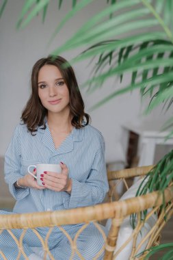 Sevimli genç erkek çizgili yerli kostüm giymiş güzel görünüme sahip, sıcak içecek içecekler, hasır koltuğa oturur, dinlenme ve izin günü sahiptir. Kişi, yaşam tarzı ve eğlence zaman kavramı