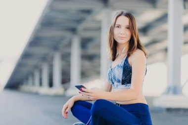 Hoş fotoğraf çekici sportif kadın geçti oturur bacaklar, arıyorsunuz en iyi giyinmiş ve tozluk, tutar modern cep telefonu, kulaklık, pozlar açık olarak canlı müzik hoşlanır. Eğlence kavramının