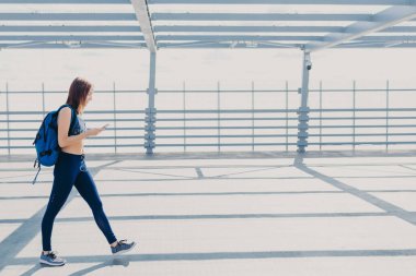 Sportif aktif kadın genç ya da genç, giyer üst, tozluk ve spor ayakkabı, taşır sırt çantası, tam uzunlukta portresi olarak hoş müzik hoşlanır, modern cep telefonu ve kulaklık kullanır