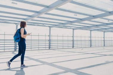 Sportclothes ve spor ayakkabı, taşır sırt çantası, sportif genç kadın arkadan görünüm güncel cep telefonu kullanır, bir yerde yürür, sağlıklı bir yaşam tarzı vardır, hoşlanır boş zaman ve yüksek hızlı internet