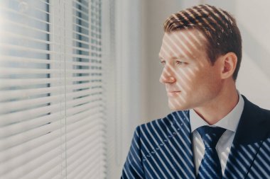 İnsanlar ve kariyer kavramı. Zengin elbiseli genç girişimci düşünüyor onun şirketin geleceği hakkında ofis pencere standları, düşünceli görünüm yoğunlaşmıştır. Erkek Genel Müdür dolapta kapalı