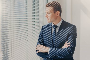 Düşünceli erkek yönetmen katlanmış silah tutar, gelecekteki iş planları hakkında düşünüyor, onun şirket yüksek kar hakkında rüyalar, düşünceli ofis pencere resmi şık takım elbise giymiş, bakar