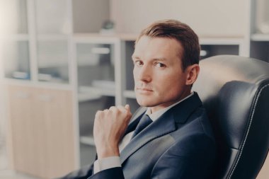 Resmi kıyafetli profesyonel erkek Yöneticisi doğrudan kameraya benziyor, sandalye, iş yerinde, yeni iş projesi hakkında conemplates aittir. Zarif adam yönetmen kendi şirket veya firma çalışır