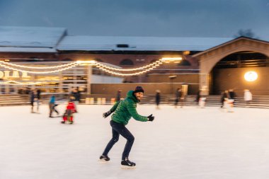 Cheerful bearded man spends Christmas time on majestic ice rink decorated with lights, skates on ice, has fun, enjoys his hobby and snowy winter weather. People, leisure, active lifestyle concept