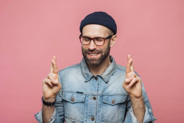 Memnun bakışla olumlu tıraşsız erkek parmak geçerek, gözleri kapalı tutar, arzu ve modern giyimleri, pembe bir arka plan üzerinde izole için daha iyi, giyer umut büyük vardır. İnsanlar ve arzu kavramı