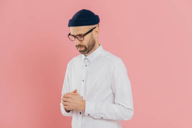 Düşünceli tıraşsız adam tutar aşağı bakışları, giyer beyaz gömlek, şapka ve gözlük, derin düşünceler, varlık çözüm yapmaya çalışır, düşünüyor, ne kadar pembe arka plan üzerinde izole işini geliştirmek