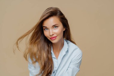 Çekici genç kadın portresi rüzgarda süzülen açık renk saçlara, doğal güzelliğe sahiptir, makyaj yapar, şık bir gömlek giyer, kahverengi arka planda izole edilir, sağlıklı bir teni vardır. İnsanlar, tarz, feminizm