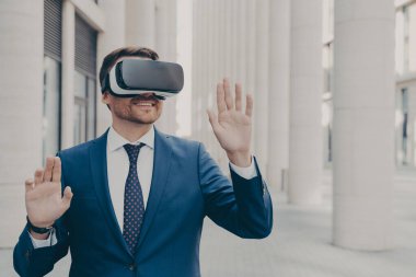 Profesyonel erkek mimar artırılmış gerçeklik kulaklığı takıyor ve dışarıda dururken gülümsüyor, iş ve iş için 3D gözlük kullanan heyecanlı iş adamı, havada sanal nesneleri hareket ettiriyor.