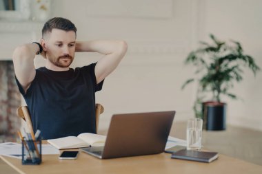 Mola verdim. Rahat poz veren, sıradan kıyafetler giyen, video izleyen ya da ev ya da modern ofis ortamından çalışırken dizüstü bilgisayardan bilgi okuyan serbest çalışan erkek ya da girişimci