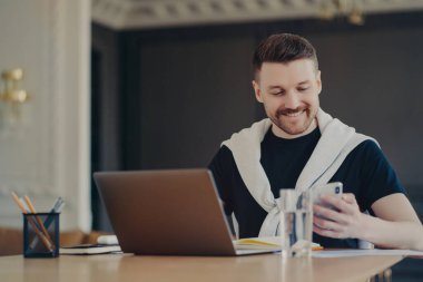 Başarılı, serbest giyinen, akıllı telefona bakıp gülümseyen, mesajları ya da iyi haberleri okuyan, evdeki dizüstü bilgisayarının önünde iş yerinde oturan yakışıklı bir erkek. İş ve iş kavramı