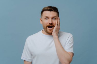 Beyaz gömlekli genç heyecanlı adam şaşırmış yüz ifadesiyle kameraya bakıyor, ağzını açık tutarken olumlu haberler alıyor, şaşırmış bir adamın stüdyo portresi. İnsan duyguları kavramı