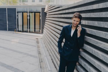 Genel müdür erkek ofisin girişinde hoş bir telefon konuşması yapıyor. Marbale çizgili dış duvara yaslanıyor. Mobile 'da yaklaşan yönetim kurulu toplantısı hakkında haber yapıyor.