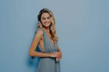 Stüdyo portresi, uzun sarı dalgalı saçlı, yumuşak mavi gece elbisesi ve koyu yakalı, pastel mavi arka planda fotokopi çeken güzel bir kadın modeli.