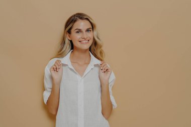 Pozitif ifade etmek. Genç, mutlu, güzel, sarışın, beyaz tişörtlü, neşeli bir şekilde gülümseyen ve neşeli bir yüz ifadesiyle kameraya bakan stüdyo duvarında izole bir şekilde poz veren güzel bir kadın.