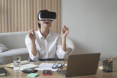 VR kulaklıklı olumlu kadın girişimci ev ofisinin masasında oturmuş uzaktan çalışırken 3D görselleştirmeyle etkileşimde bulunuyor. Modern IT ürün testi dijital simülatör kavramı üzerine