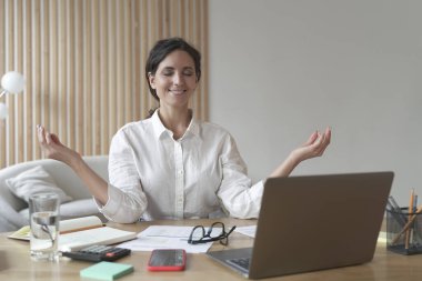 Sakin sakin kadın meditasyon yapıyor, Zen pozisyonunda otururken yoga yapıyor, yoğun çalışma gününden sonra nefes egzersizleri yapan mutlu iş kadını gülümsüyor.