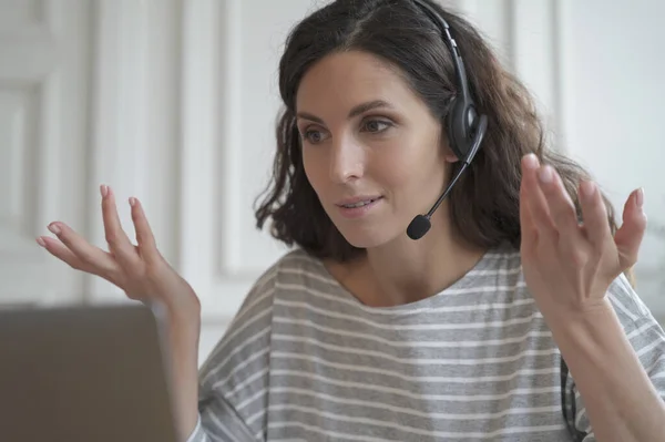 Confident focused young spanish businesswoman wearing wireless headphones having video call conversation with partner or giving professional consultation, consulting customer online