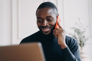 Afrika kökenli neşeli genç bir adam. Ticaret şirketi sahibi, ev ofisinden bilgisayardaki ürünleri karşılaştırırken ve kontrol ederken siparişleri onaylamak için tedarikçiyi arıyor.