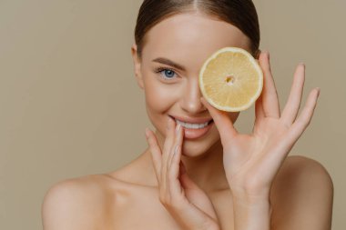 Güzel bir bayan modelin kapalı çekimleri taze ve sağlıklı cilde sahiptir. Göz kapakları turuncu pozlarla kaplıdır. Bej arka planda izole edilmiş çıplak omuzlar. Yüz maskesi yapmak için gerekli