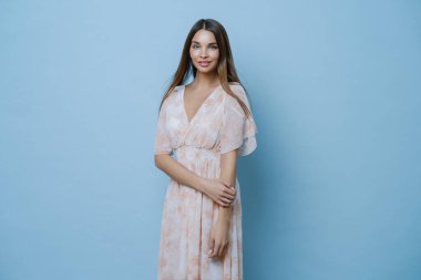 Romantik bir yaz randevusuna çıkmaya hazır, uzun ipek elbiseli, çekici bir yüzü, zarif bir görünüşü var, mavi arka planı var, parti için giyinmiş..