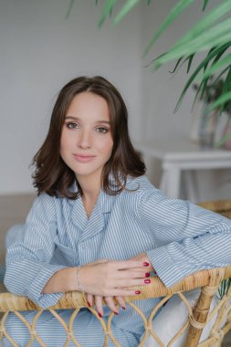 Hoş dikey çekim-hasır sandalye, çizgili ceketi, giyinmiş genç Avrupa koyu saçlı kadın oturur seyir kırmızı manikür vardır, yakışıklı kamera göz yakaladı, karşı iç iç teşkil etmektedir.