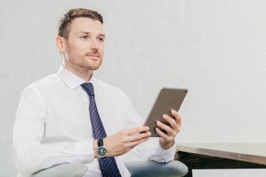 Düşünceli beyaz erkek laywer bir şey hakkında düşünüyor, modern tablet bilgisayar tutar, beyaz gömlek siyah kravat giyer, kabine, istemci için bekler oturur. İnsanlar, iş, teknoloji kavramı