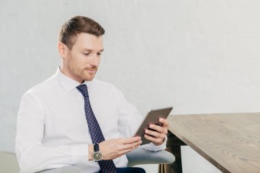 Yakışıklı genç başarılı erkek fiinancier yatay atış modern tablet bilgisayar kullanır, beyaz gömlek kravat takıyor, işten sonra sonu vardır, kabine, okuma bilgi tahta masada oturur