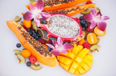 Beyaz arka planda taze organik egzotik meyveler. Olgun dargon meyve, papaya, kivi, kumquat ile mango, güzel orkide ile dekore.