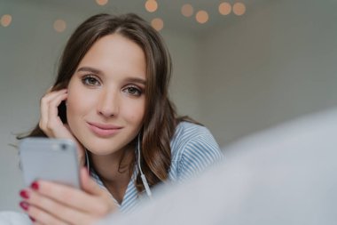 Oldukça koyu saçlı kadın spneds serbest zaman en sevdiği şarkıyla samimi shot modern cep telefonu tutan, doğrudan kameraya benziyor, kapalı teşkil etmektedir, yapmak vardır. Çekici kız yeni melodiler arar