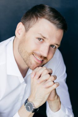 Dikey dostu gülümsemeyle yakışıklı neşeli tıraşsız erkek portresi palms birlikte basıldığında çene altında tutar, izle yandan giyer, kameraya mutlu görünüyor. Profesyonel genç adam işçi