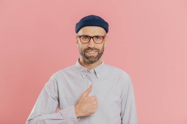 Memnun çekici adam çekici bir görünüme sahiptir, başparmak yükseltir, bir şey ile gülümseyerek mutlu bir şekilde kabul eder, şapka ve pembe arka plan üzerinde izole tişört giyiyor. Yakışıklı öğrenci arkadaşlar iyi fikir onayladı