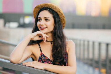 Uzun siyah kalın saç konumu köprüsünde rüya gibi ifade mesafe içine arıyorum yaz şapka ve açık havada dinlenme elbise giyen sahip olan genç kadın modeli. İnsanlar, gevşeme, güzellik kavramı