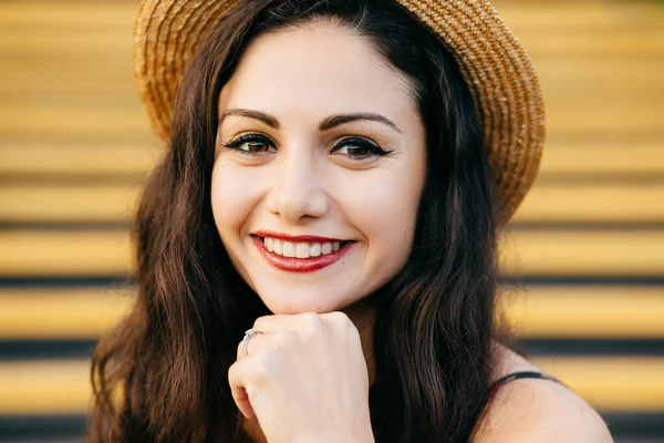 People, beauty, emotions concept. Close up portrait of beautiful brunette female with nice make-up and thin red lips smiling gently demonstrating her white teeth while keeping her hand under chin