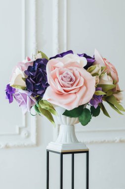 Yapay çiçek çiçek stand ve uzun vazo dekorasyon nesnesi olarak kullanılan geniş salonda beyaz arka plan üzerinde dikey atış.