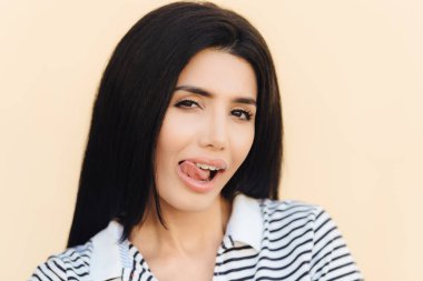 Portre çekici kadın modeli ağız diliyle yalıyor, meraklı görünüm, sağlıklı cilt ve siyah saçlı, kurnaz ifade, stüdyo duvardan izole vardır. Yüz ifadeleri ve güzellik kavramı