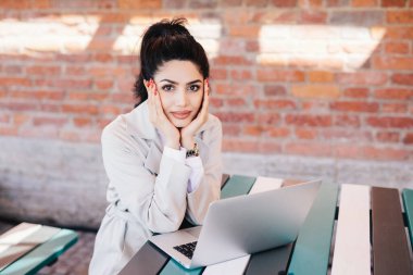 Koyu saç ve makyaj, uzun kırmızı ile çekici Bayan yanaklarda kafede masada onun akraba veya arkadaşlar üzerinden görüntülü görüşme için bekleyen açık dizüstü bilgisayar önünde oturup dinlenme ellerini tutan çiviler