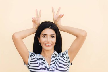 Mutlu esmer erkek portresi boynuz jest yapar, eğlenceli ve arkadaşlarınızla, keyfin yerinde olmak foolishes var, gündelik kıyafet, gülümsüyor geniş kamera, dişlerde gösterir diş teli takıyor. Komik kadın kapalı